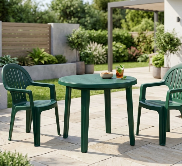 Compamia Ronda Resin Round Dining Table – Green Table with Stacking Chairs Compamia Ronda Resin Round Dining Table paired with two matching green resin armchairs on a backyard patio, set near a pergola and garden beds.